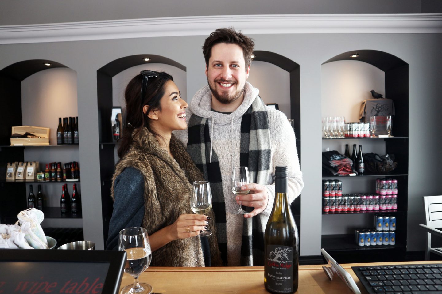 A smiling couple hold glasses inside a wine shop.