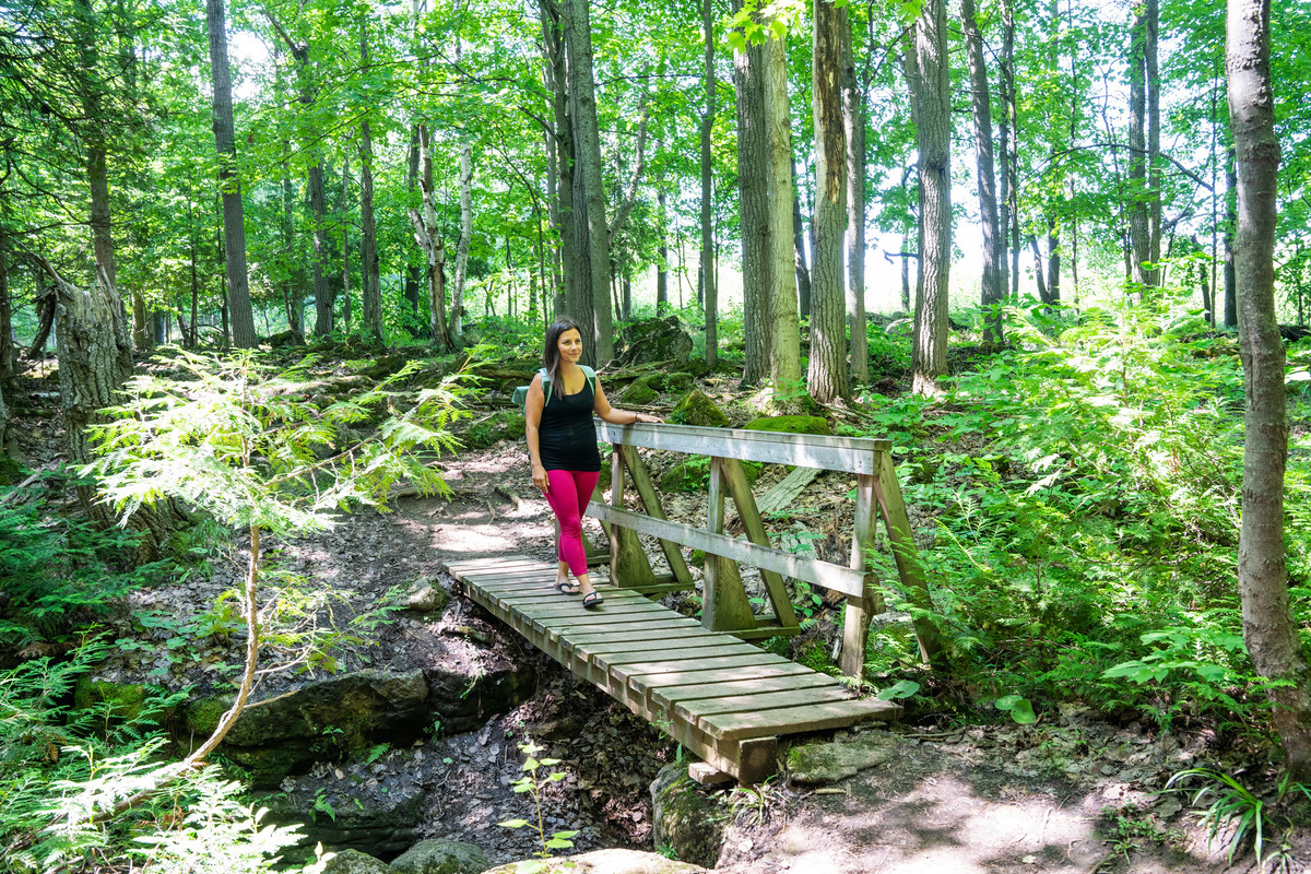 Woman walking across wooden foot bridge in forest while on a hike