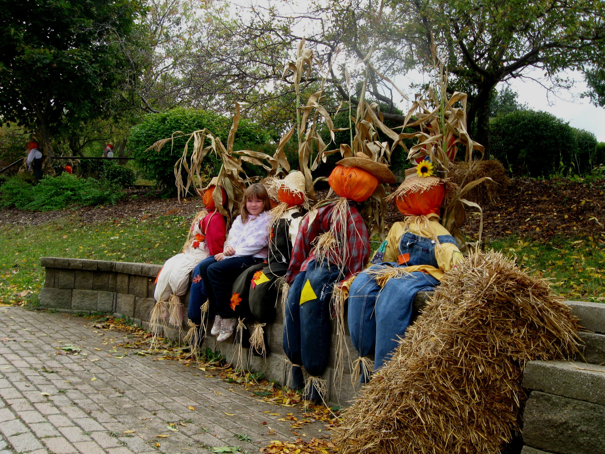 A child sits beside several scarecrows on a stone wall.