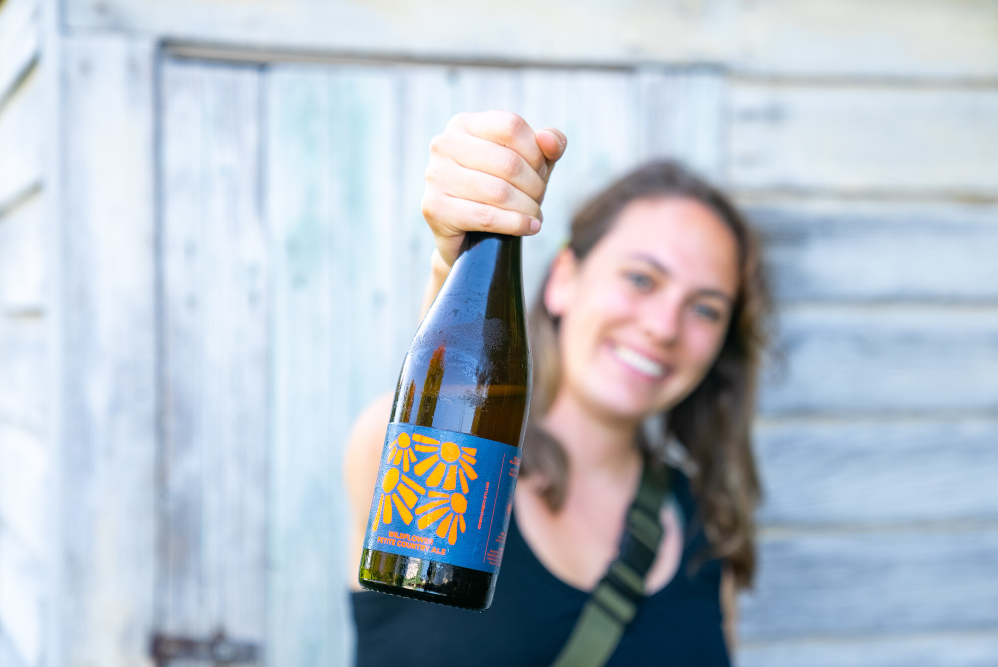 Smiling person holds a bottle of wine or cider.