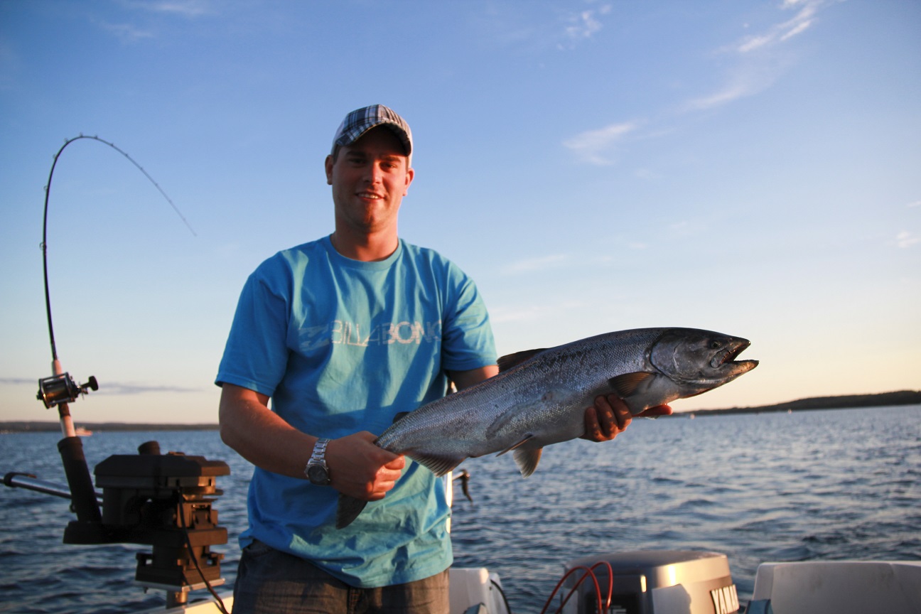 A fisherman on a boat proudly holds up a fish.