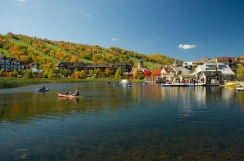Kayaks and paddleboats on a body of water beside chalets beneath a hill.