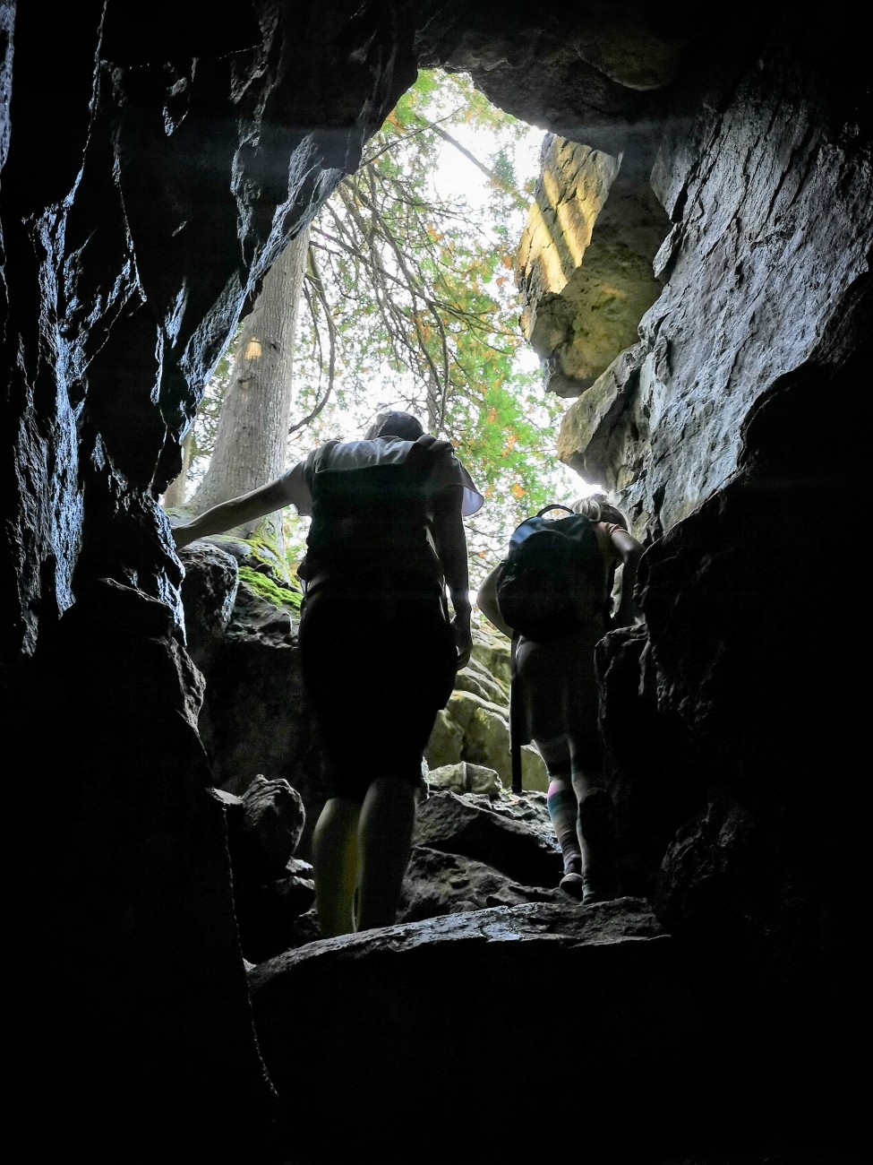 Two people are silhouetted climbing out of a cave.