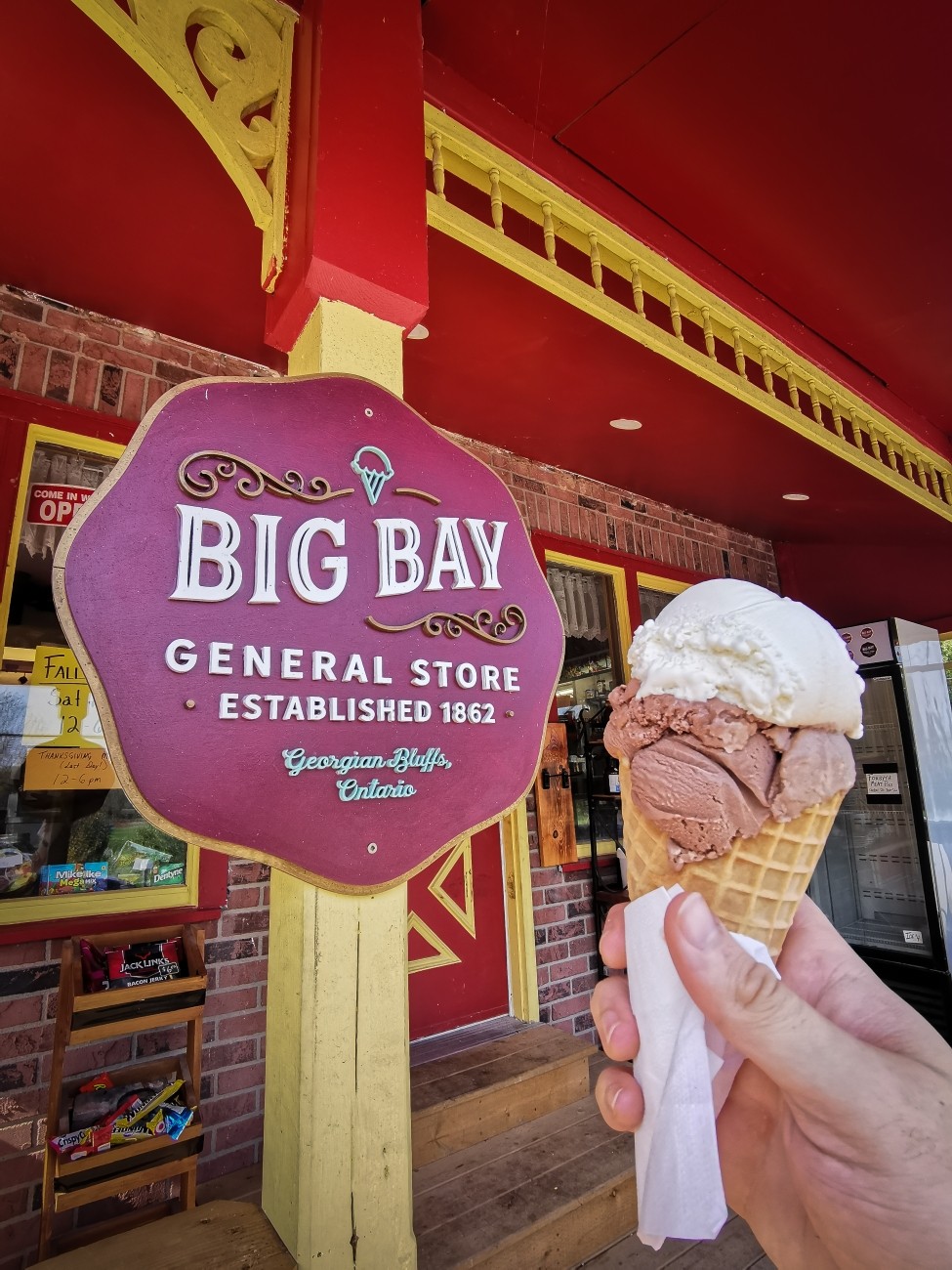First person point of view of a hand holding an ice cream cone in front of a store.