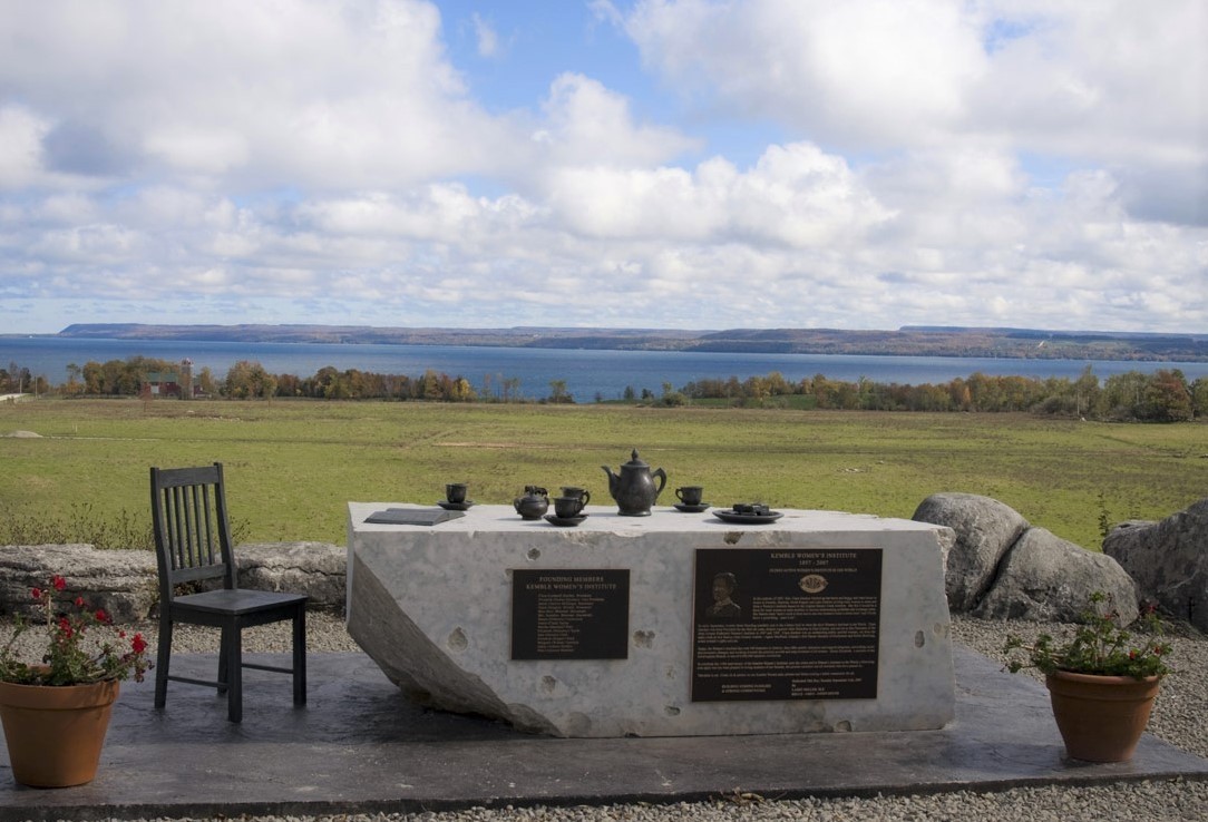 A monument featuring a chair and a tea set arranged on a large rectangular stone.