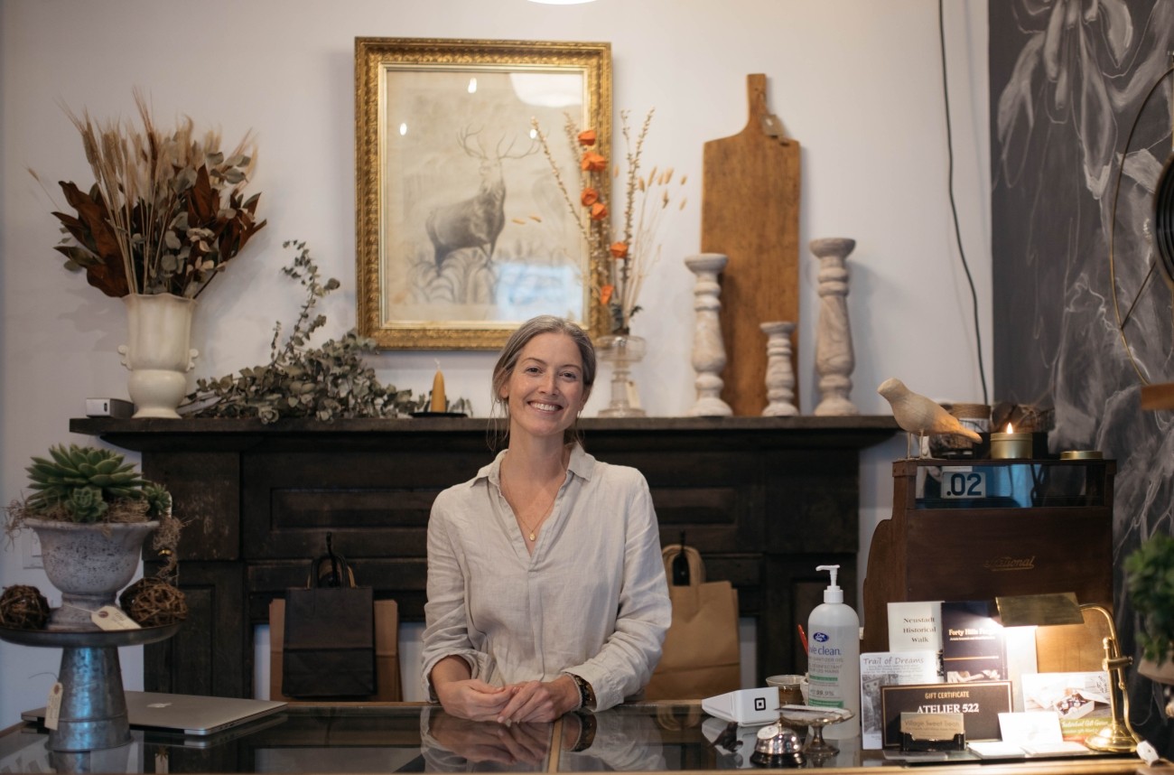 A smiling woman behind a counter in a boutique store.