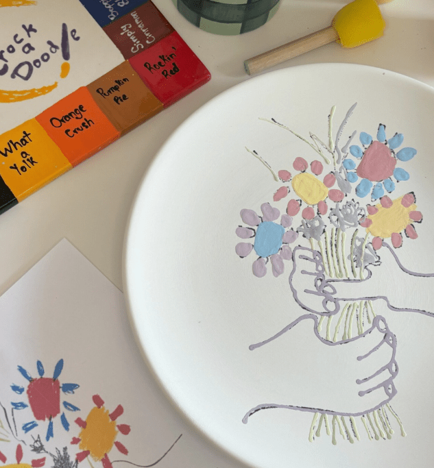 A hand painted plate with hands grabbing flowers