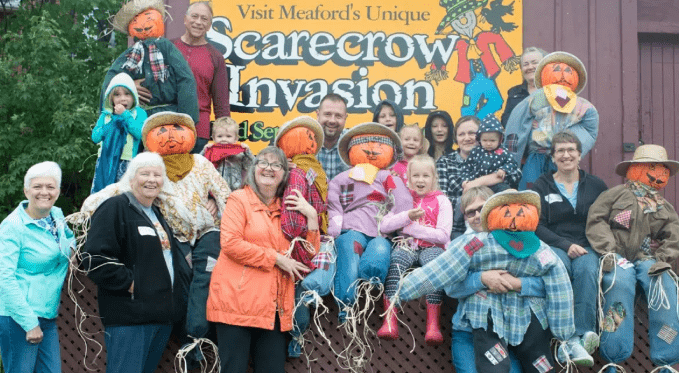 A group of people pose with several scarecrows.