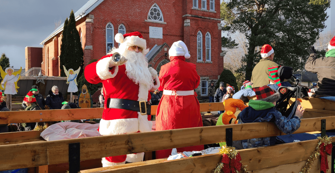 Santa stands aboard a float ringing a bell during a parade.