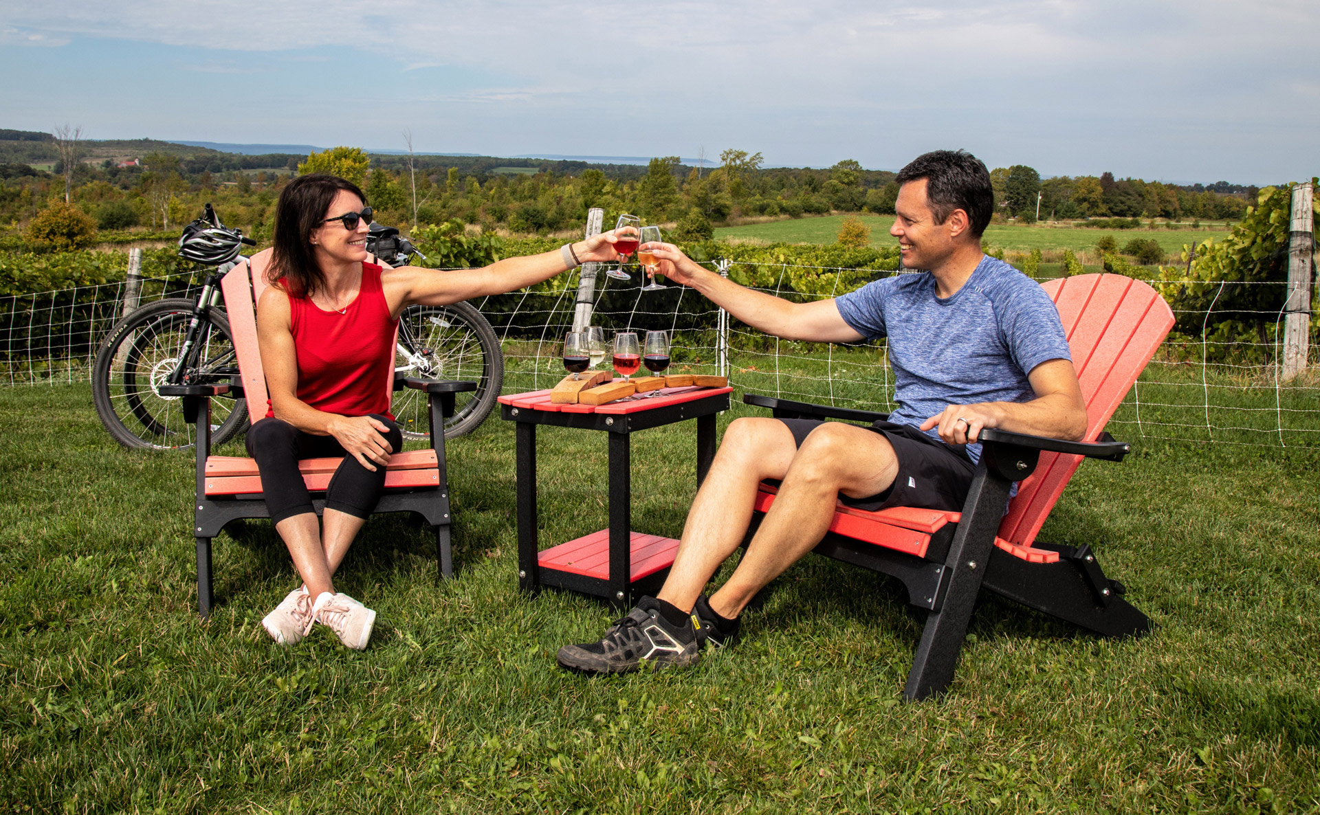 Two people seated outside raise glasses to each other. A vineyard stretches out behind them.
