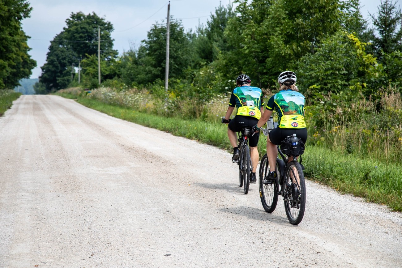Two people in matching shirts cycle a gravel road together.